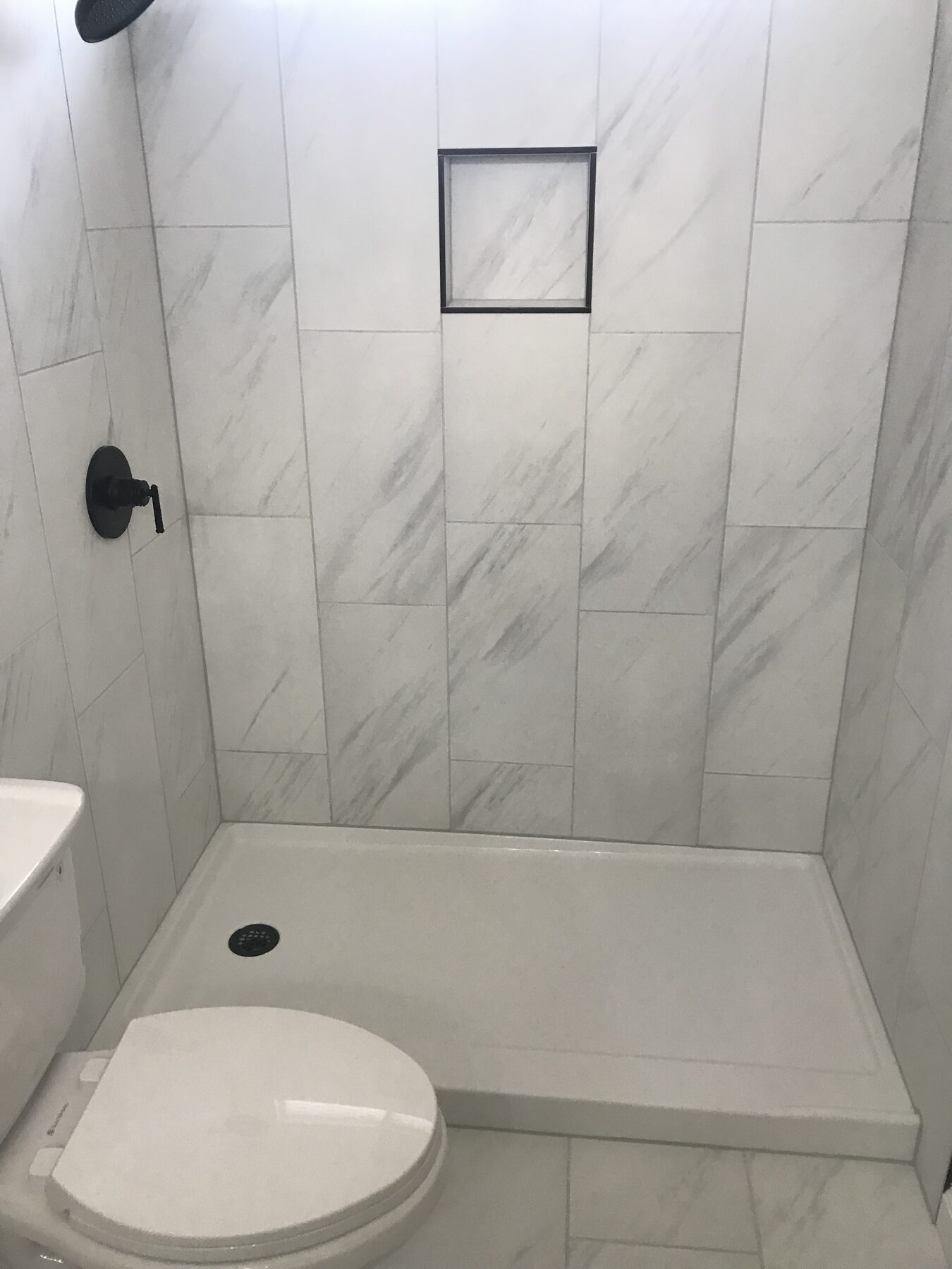 Walk-in shower in large marble-look tile with matte black fixtures and a built-in niche