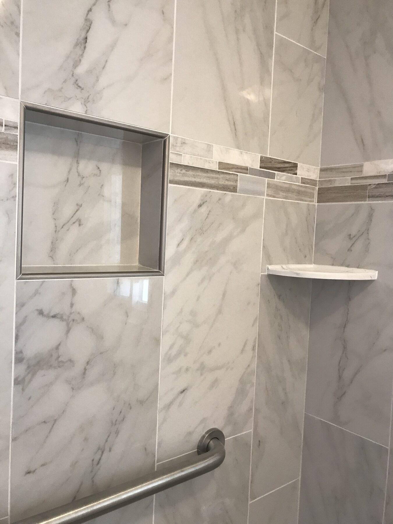 Shower niche close-up with marble tile, a mosaic accent band and a grab bar