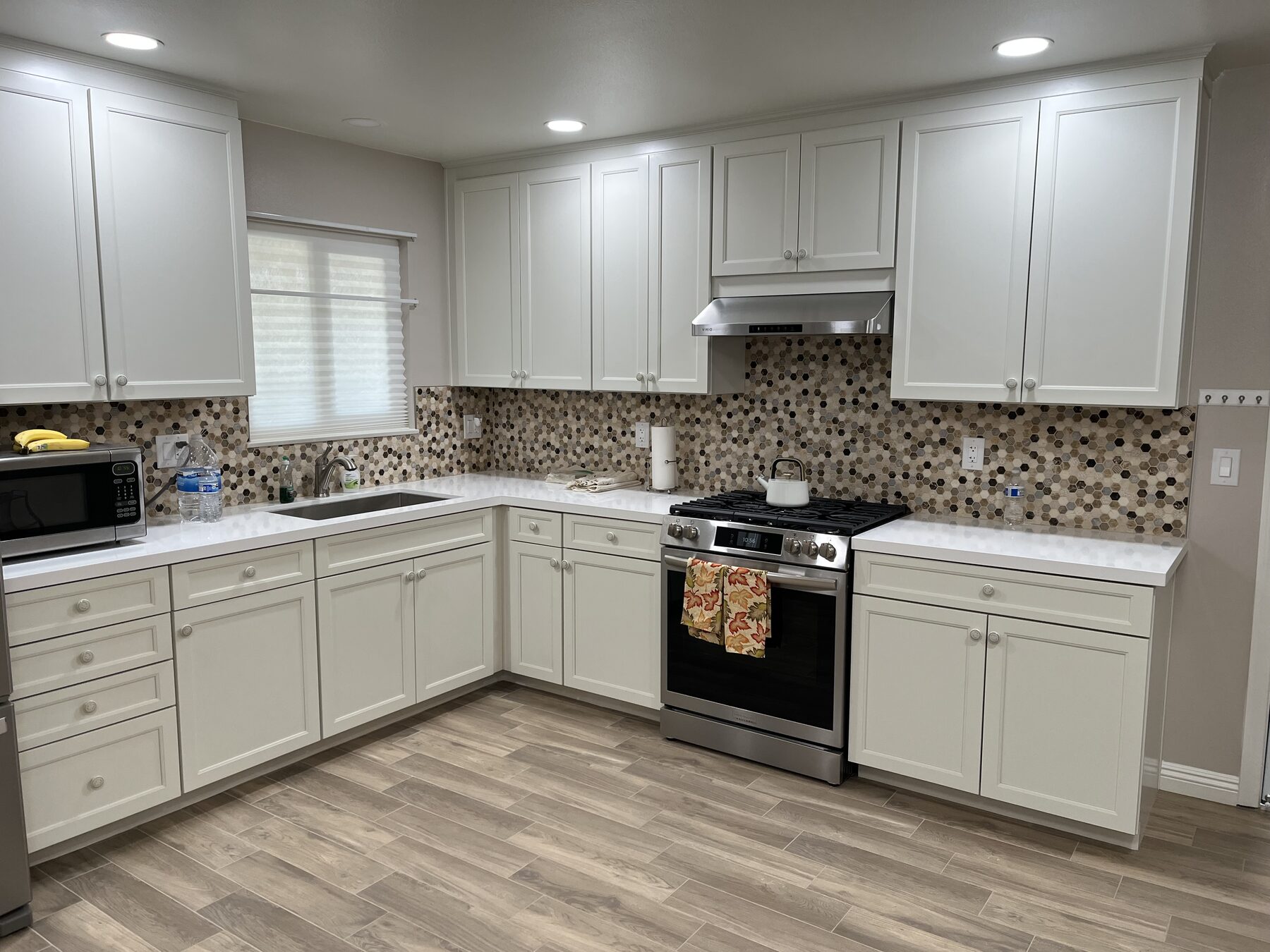 Remodeled kitchen with white shaker cabinets, mosaic tile backsplash, wood-look plank floor, stainless range and recessed lights