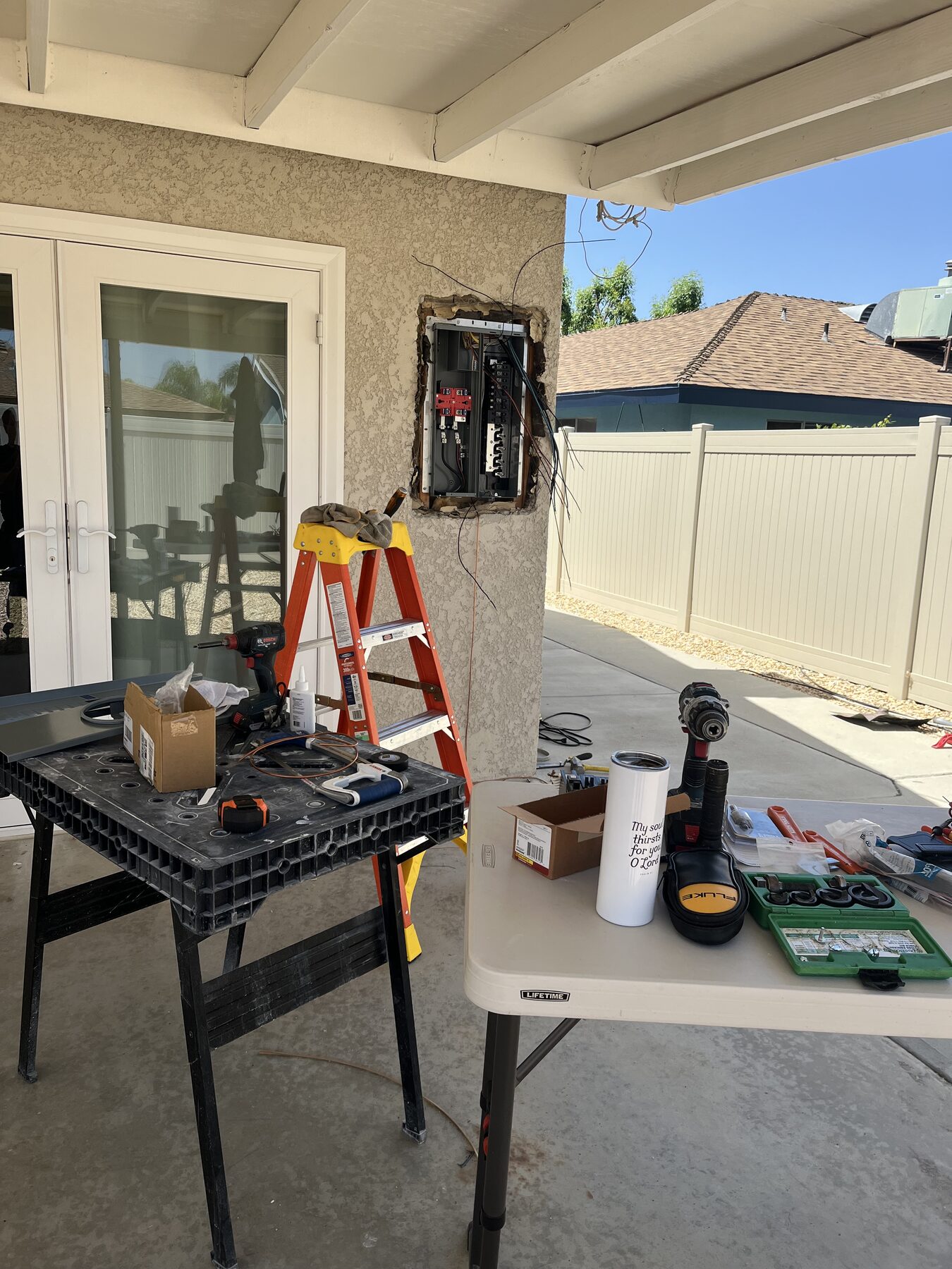 Job in progress on a back patio: ladder, tools on a folding table and new French doors