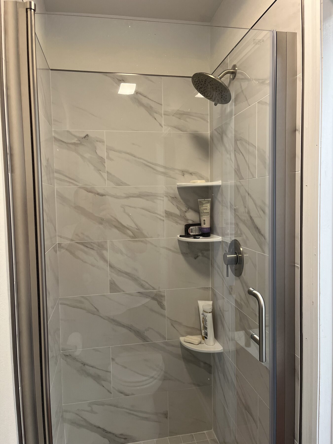 Frameless glass shower enclosure with marble tile and a rainfall shower head